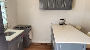 Cozinha compacta com armários cinzas, bancada branca, fogão a gás e luminária pendente.
