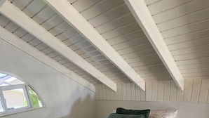 Uma cama de solteiro com um edredom verde, um travesseiro branco e um travesseiro verde escuro num quarto com soalho de madeira e teto inclinado.