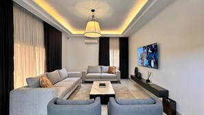 A modern living room with a sofa set, a coffee table, and a TV mounted on the wall. - The Barli Hotel and Apartments (Abuja)