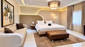 Una habitación de hotel moderna con una cama grande, un sofá, una mesita de noche y un cuadro en la pared.