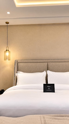 A hotel room with a bed, a bedside table, a nightstand, a framed welcome sign, and a hanging light fixture. - The Barli Hotel and Apartments (Abuja)