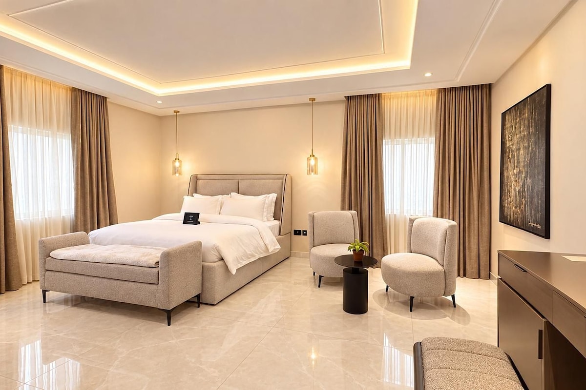 A modern hotel room with a large bed, two armchairs, a small table with a plant, and a desk.