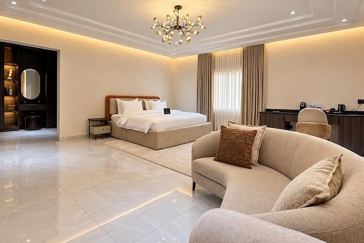 A modern bedroom with a large bed, bedside tables, a sofa, and a desk area.