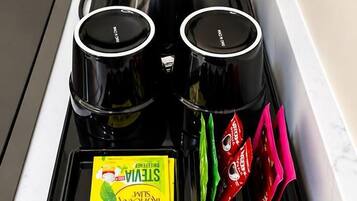 Una cafetera con un asa negra y cuerpo de acero inoxidable, conectada a una toma de corriente.