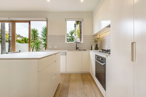 Eine moderne Küche mit weißen Schränken, einem eingebauten Ofen und einem Fenster mit Blick auf einen Garten.