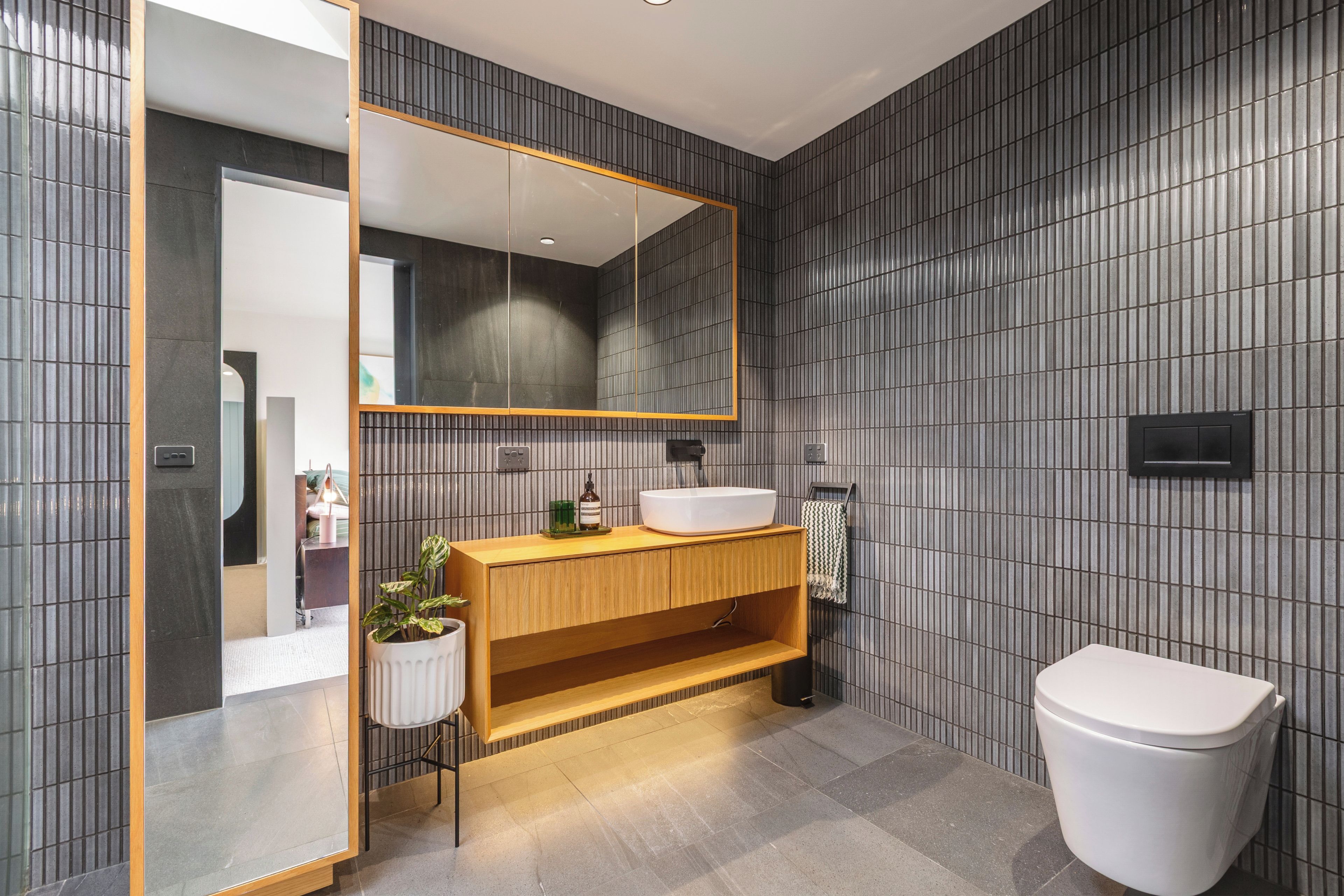 Ein modernes Badezimmer mit einem Holzwaschtisch, einem großen Spiegel und einer weißen Toilette.