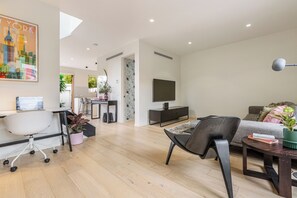 Ein modernes Wohnzimmer mit Flachbildfernseher, einer Couch, einem Couchtisch und einem Schreibtisch mit Computer.