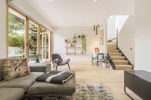A modern living room with a sofa, a chair, a coffee table, and a staircase leading to an upper level. - Bayside Grove The Heart of St Kildas Coastal Life (Saint Kilda)
