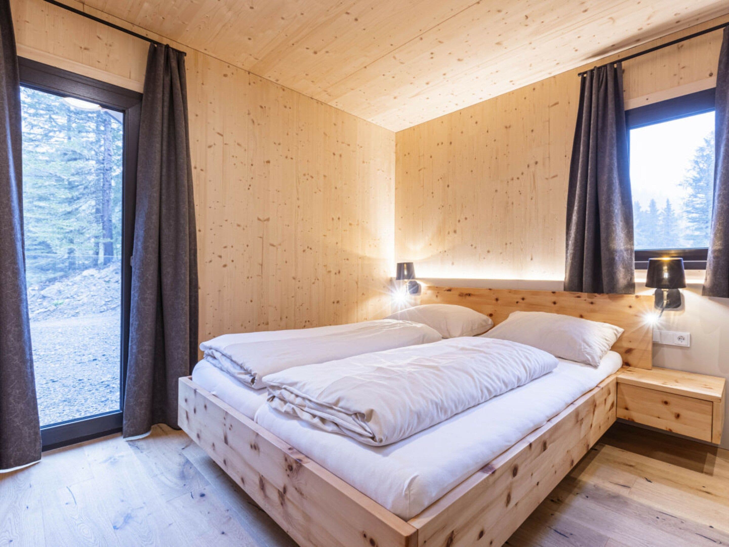 Une chambre dans une cabane en bois, avec un lit, des tables de chevet et une fenêtre avec des rideaux.