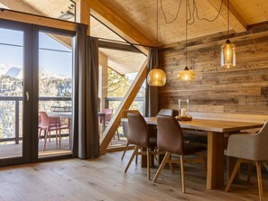 A dining area with a wooden table, chairs, and pendant lights. - Superior Chalet #1 With Sauna & Hot Tub (Stadl-Predlitz)