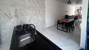 A kitchen with a gas stove and sink, a dining area with a table and chairs, and a hallway leading to a living space. - Lençóis Maranhenses House (Barreirinhas)