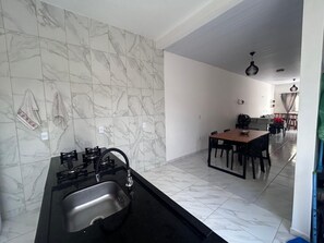 A kitchen with a gas stove and sink, a dining area with a table and chairs, and a hallway leading to a living space. - Lençóis Maranhenses House (Barreirinhas)