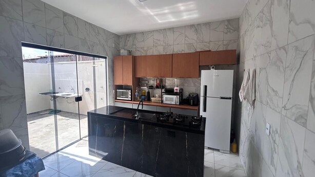 A modern kitchen with a black island, wooden cabinets, and a large window. - Lençóis Maranhenses House (Barreirinhas)