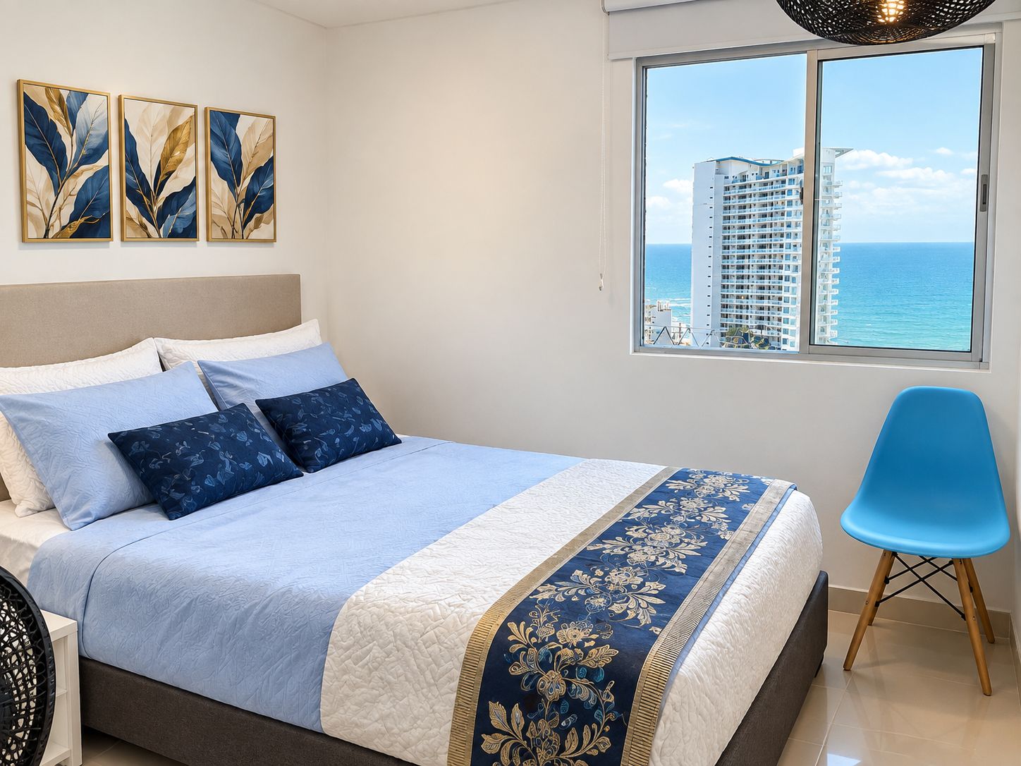Un dormitorio con una cama, un ventanal con vistas a edificios y al mar, y una silla azul.