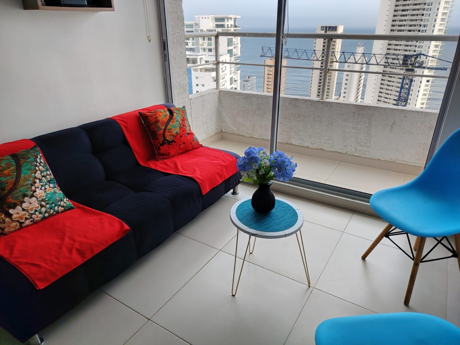 Een balkon met een bank, een kleine tafel met een vaas en een blauwe stoel.