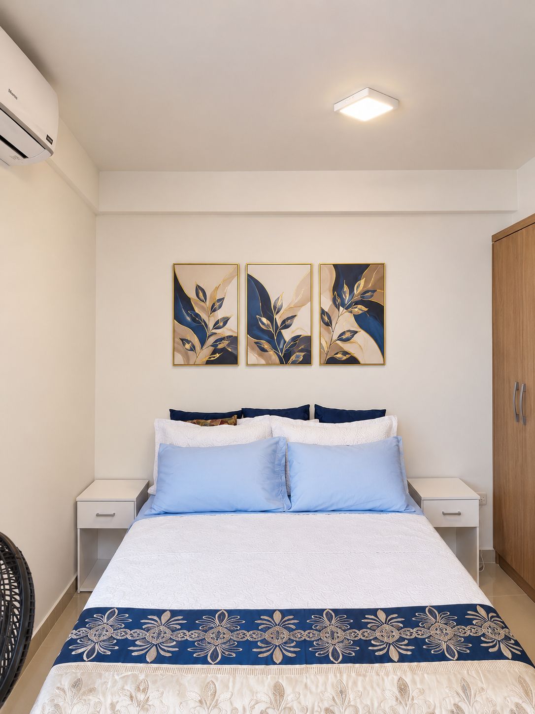 A bedroom with a bed, two bedside tables, a wardrobe, and three wall-mounted artworks.