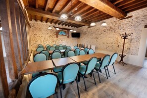Ein Konferenzraum mit langem Tisch und Stühlen, Steinwänden, Holzbalken und Deckenleuchten.