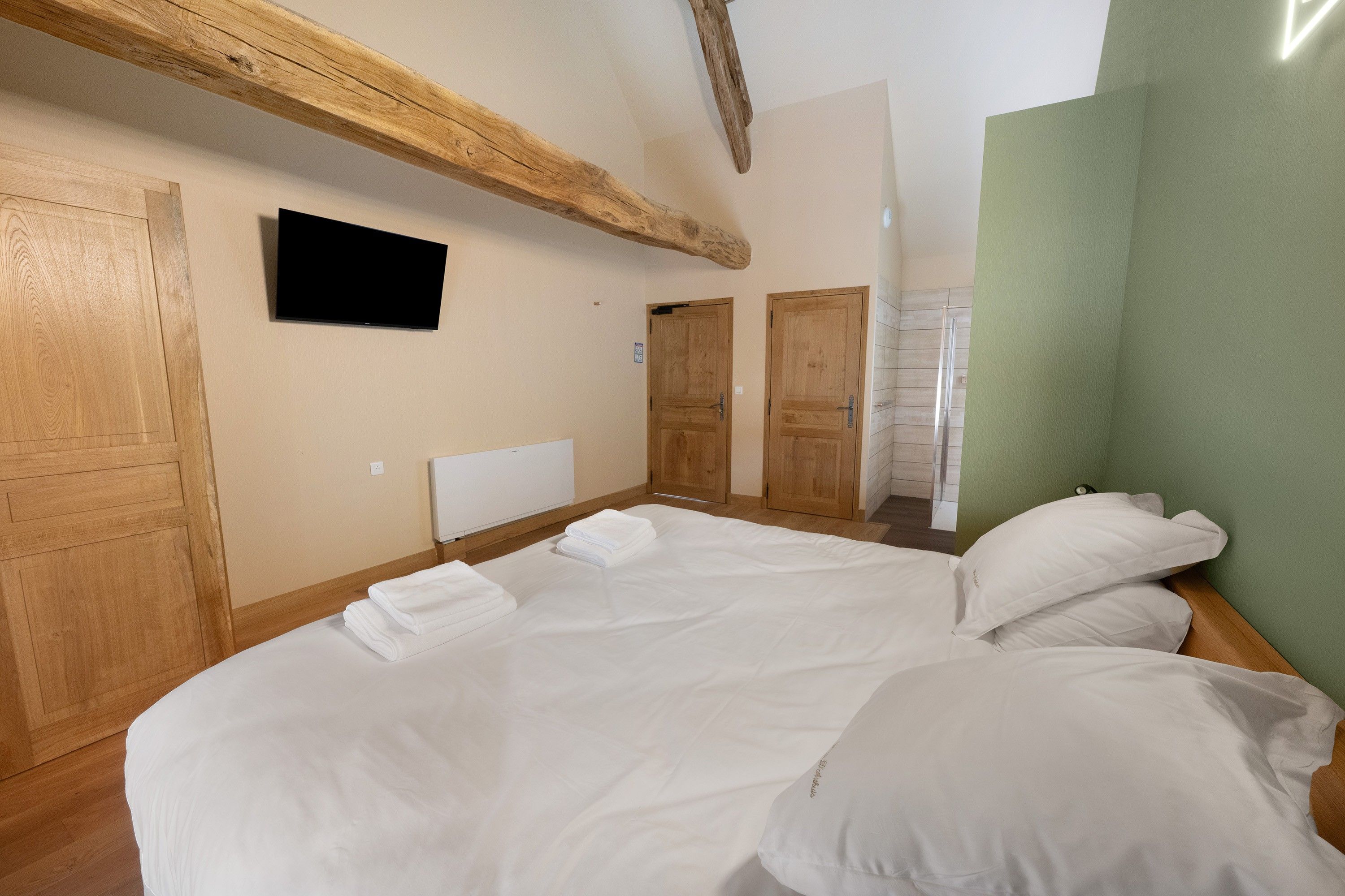 A bedroom with a large bed, wooden beams, a flat-screen TV, and a green accent wall.