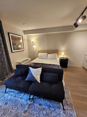 A modern bedroom with a bed, a sofa, a bedside table, and a wall-mounted lamp. - Modern Studio with Queen Bed in Raleigh (Raleigh)