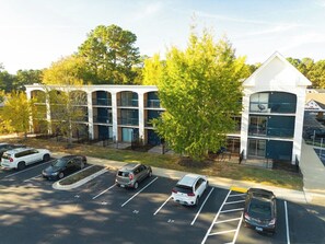 A multi-story parking structure adjacent to a building with a white facade and a green tree in the foreground. - Modern Studio with Queen Bed in Raleigh (Raleigh)