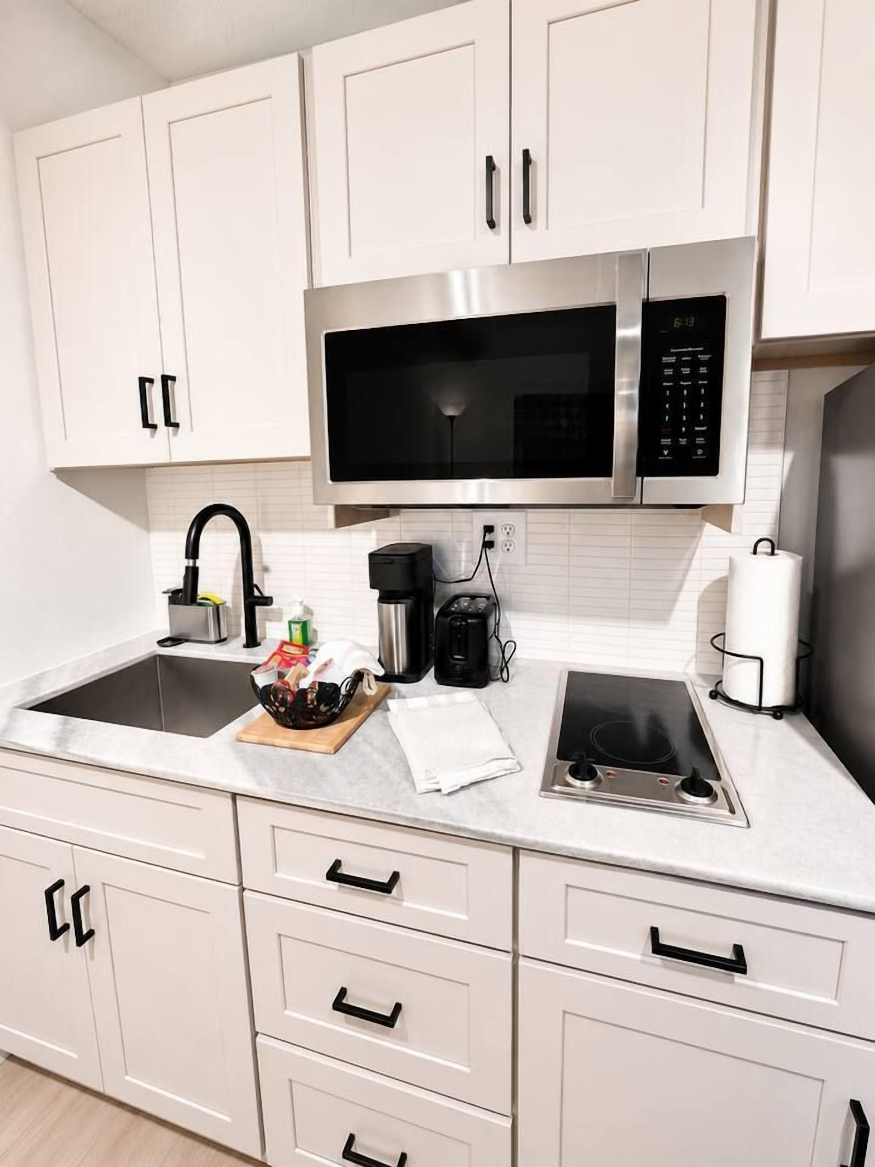 Una cocina moderna con armarios blancos, microondas de acero inoxidable, cafetera y estufa a gas.