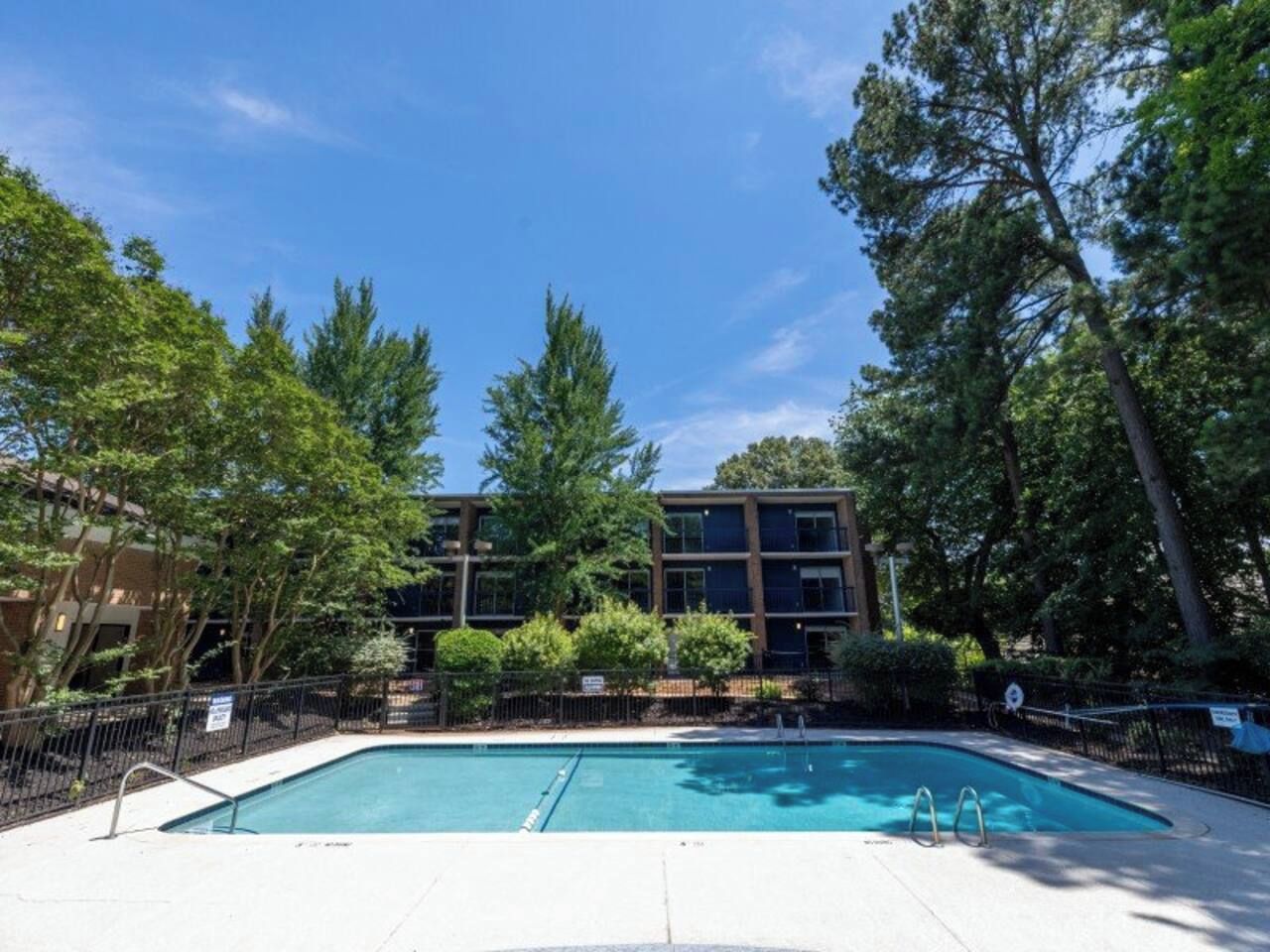 A rectangular pool with a metal ladder, surrounded by a fence and trees.