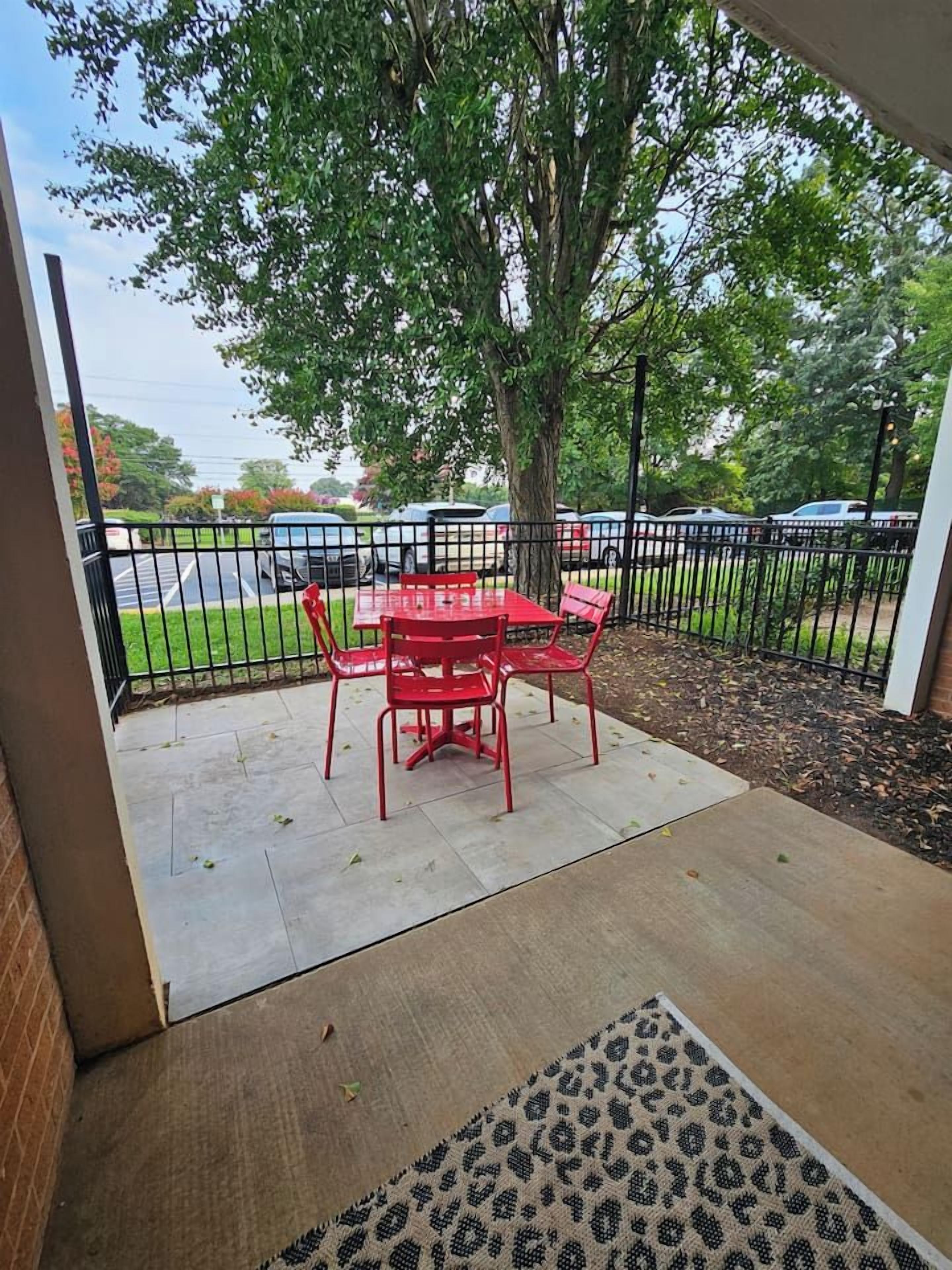Une terrasse extérieure avec une table et des chaises, un arbre et une vue sur un parking.