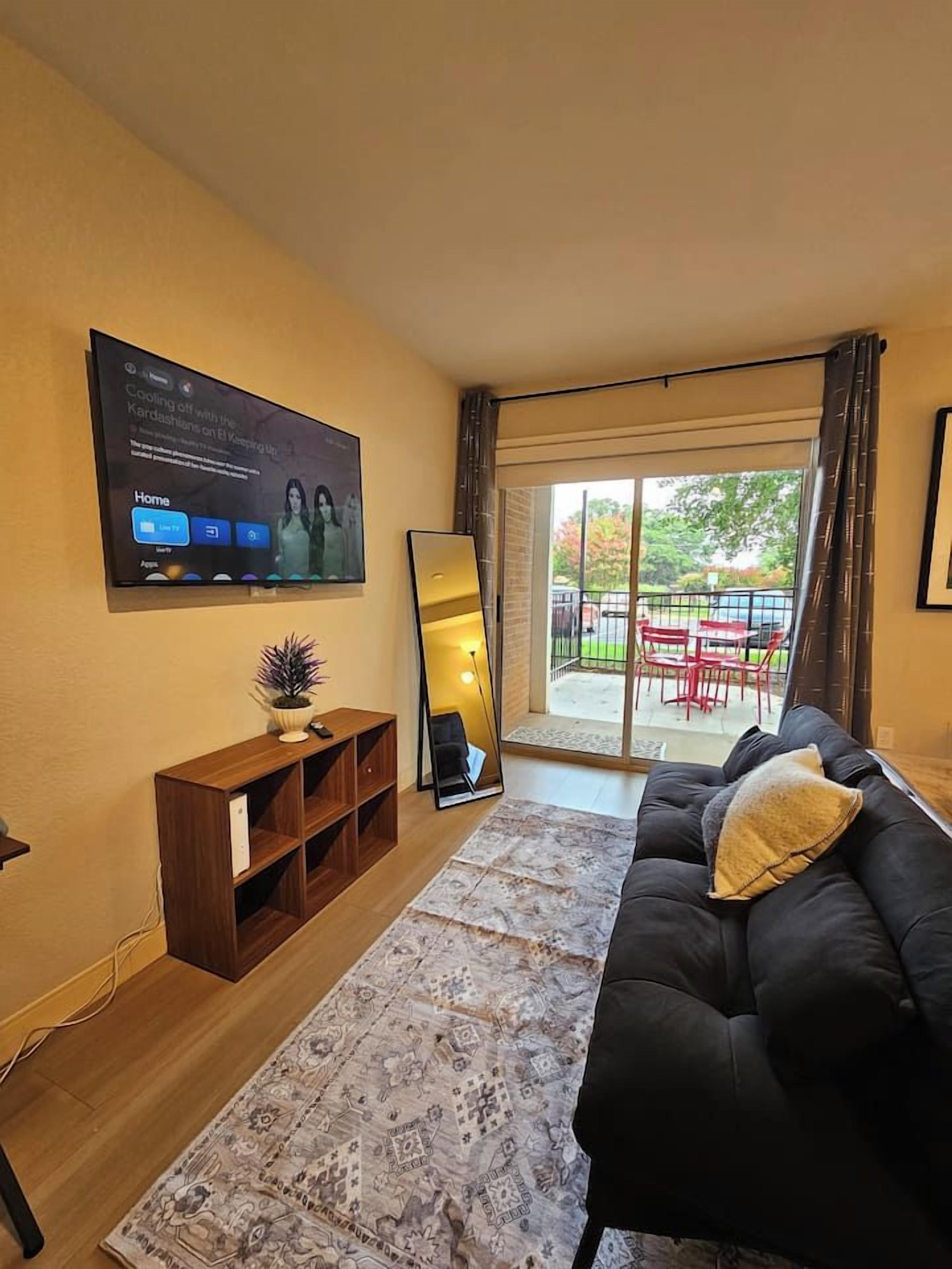 A living room with a sofa, a flat-screen TV mounted on the wall, a wooden entertainment unit, and a large mirror.