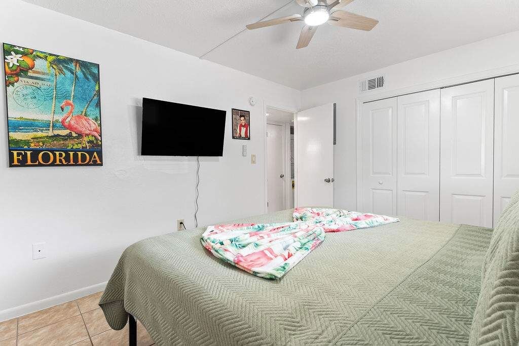 Ein Schlafzimmer mit Bett, Deckenventilator, Fernseher, einem Poster von Florida und einem Kleiderschrank.