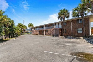 A two-story motel with a parking lot, palm trees, and a clear sky. - Flamingo Rock Three Minute Walk to the Gulf! (Okaloosa Island)