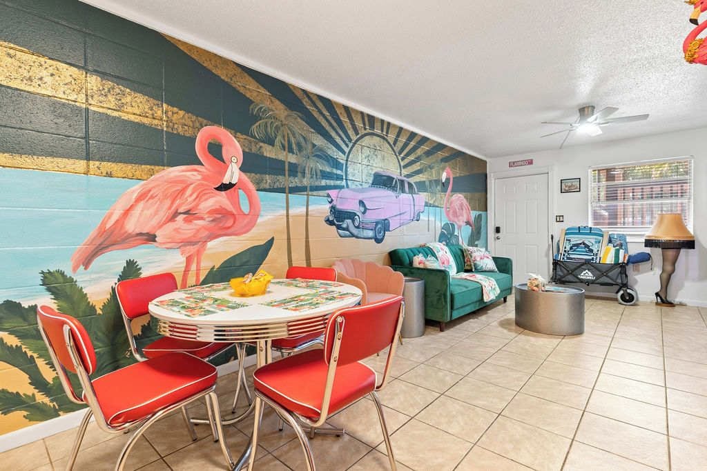 A room with a mural of a beach scene, a round table with chairs, a green sofa, and a small cart with items.