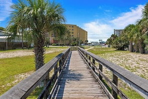 A wooden boardwalk leading to a building with a flat roof and multiple windows. - Flamingo Rock Three Minute Walk to the Gulf! (Okaloosa Island)