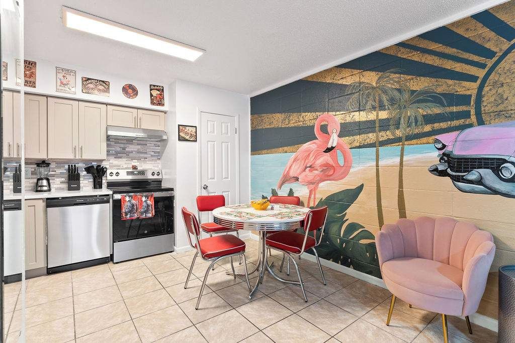 A kitchen with a dining area, a mural of a flamingo and a car, and a pink chair.