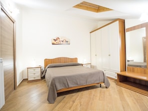 Un dormitorio con cama de madera, una mesita de noche, un armario y un aplique de techo.