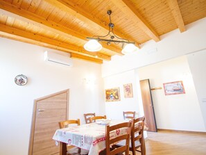 Un comedor con vigas de madera en el techo, una mesa con mantel, sillas y una obra de arte colgada en la pared.