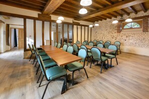 Ein Konferenzraum mit langen Tischen und Stühlen, Holzbalken an der Decke und einer Steinsäule.