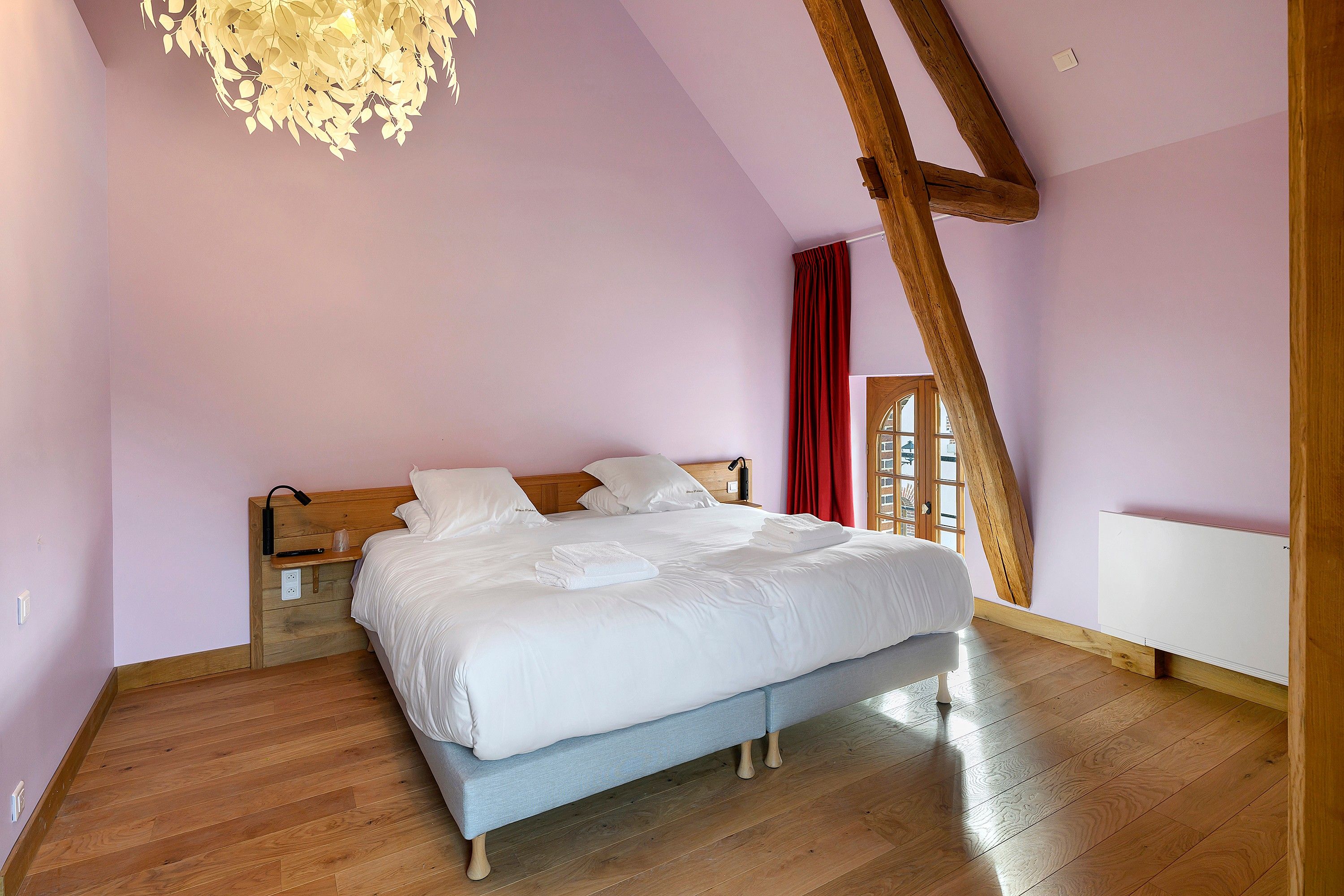 Une chambre à coucher avec un lit en bois, une table de chevet, un rideau rouge et une poutre en bois au plafond.