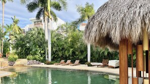 A pool area with lounge chairs, a thatched-roof structure, and tropical vegetation. - Vrbo Property (Nuevo Nayarit)