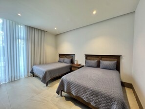 Une chambre d’hôtel avec deux lits, une table de chevet, une lampe et une grande fenêtre avec des rideaux.
