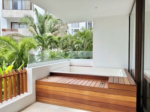 Ein moderner Balkon mit Holzboden, Glasgeländer und Blick auf Grünflächen und Gebäude.