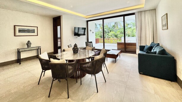 A modern living room with a dining area, a sofa, a TV mounted on the wall, and a balcony with a view of greenery. - Vrbo Property (Nuevo Nayarit)