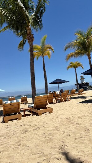 A beach with wooden lounge chairs and umbrellas, palm trees, and a clear view of the ocean. - Two-bedroom apartment in Cruz de Huanacaxtle with beach access (Nuevo Nayarit)