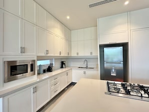 Een moderne keuken met witte kasten, een roestvrijstalen koelkast, een inbouwoven en een gasfornuis.