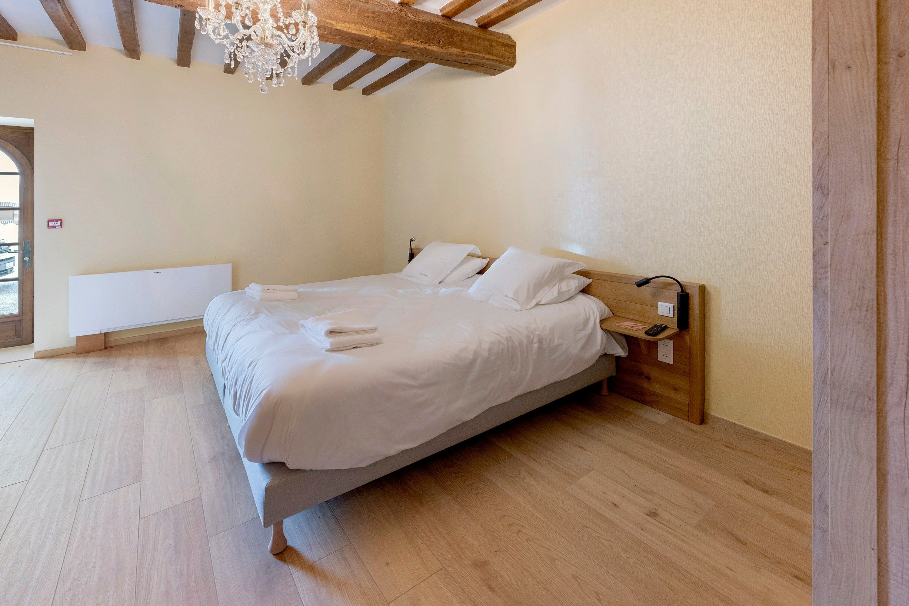 Une chambre à coucher avec une tête de lit en bois, un lit recouvert de draps blancs, une table de chevet avec une télécommande et un lustre.