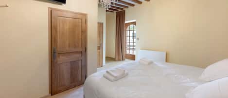 Ein Schlafzimmer mit Holztür, einem an der Wand montierten Flachbildfernseher, einer Kristallleuchtre und einem Bett mit weißer Bettwäsche.