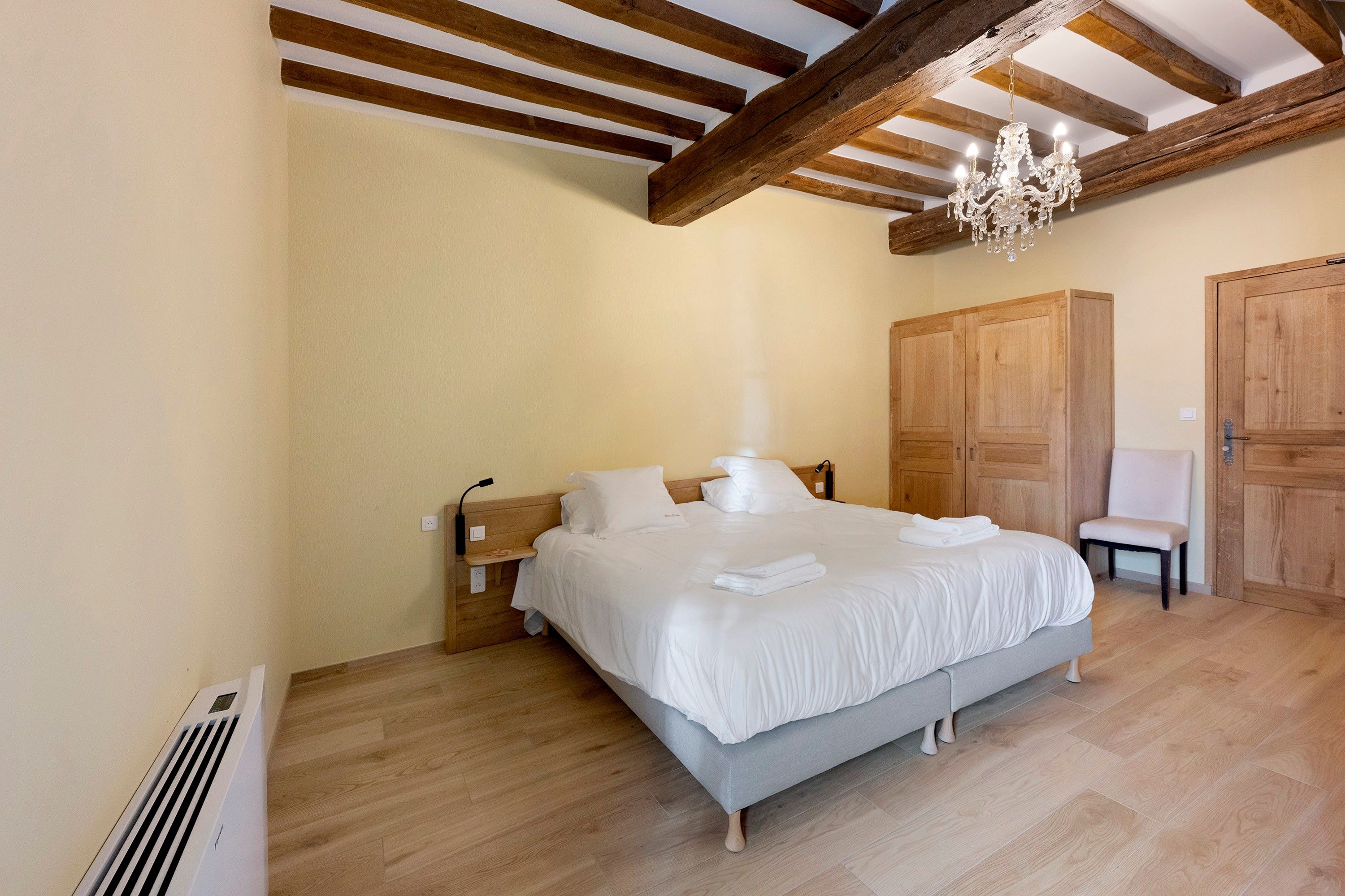 Een slaapkamer met een groot bed, een houten garderobe en een kroonluchter.