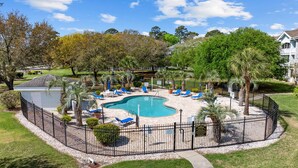 A swimming pool with lounge chairs and palm trees, surrounded by a fence. - Golf Course Gateway - 1BR - Sleeps 4 (Myrtle Beach)