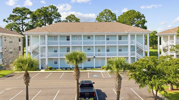 A multi-story motel with a parking lot and palm trees. - Golf Course Gateway - 1BR - Sleeps 4 (Myrtle Beach)