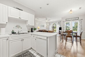 Eine moderne Küche mit weißen Schränken, einem eingebauten Geschirrspüler und einem Essbereich mit einem Holztisch und Stühlen.
