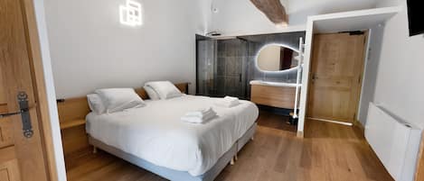 Une chambre moderne avec un grand lit, une douche intégrée et un plafond en bois.